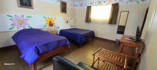 a room with two beds and a desk and a television at Kurumi Hostel in Cusco