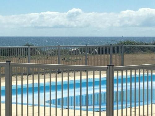 a swimming pool behind a fence with the ocean in the background at Maeva 7 in Guidel