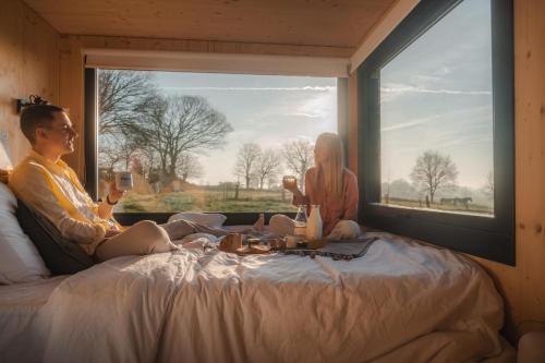 a man and woman sitting on a bed looking out a window at Parcel Tiny House Carré d'Ach, campagne près de Rennes 