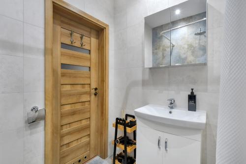 La salle de bains est pourvue d'un lavabo et d'une porte en bois. dans l'établissement Green Point Apartment, Sosnowiec City Center, à Sosnowiec