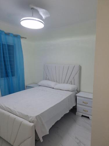 a bedroom with a white bed and a blue curtain at Residencial cayena del este Santo Domingo este in La Grúa