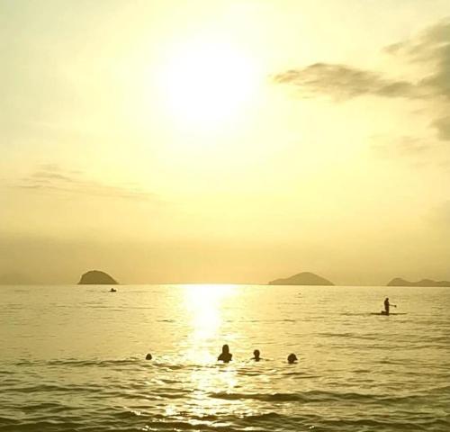 a group of people swimming in the ocean at sunset at Casa de condomínio em Boicucanga in Boicucanga