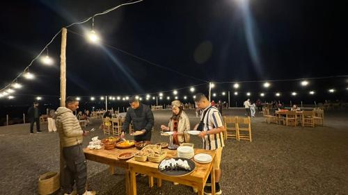 a group of people standing around a table with food at LA HACIENDA Agafay Desert 