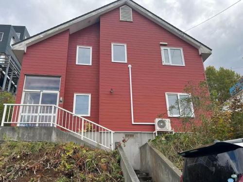 een rood huis met een witte leuning op de veranda bij 青山ハウス in Otaru