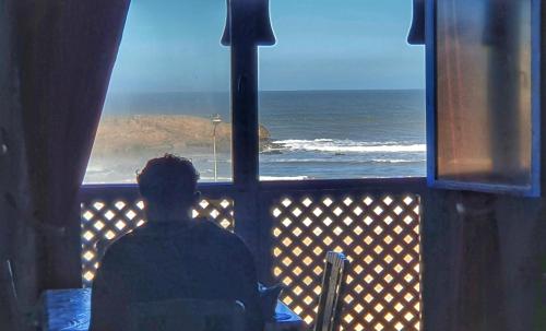 a man sitting in front of a window looking at the ocean at Ocean Hideaway - Sea View in Essaouira