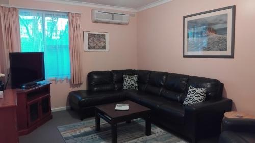 a living room with a black leather couch and a tv at Lakes Entrance Holiday Units in Lakes Entrance