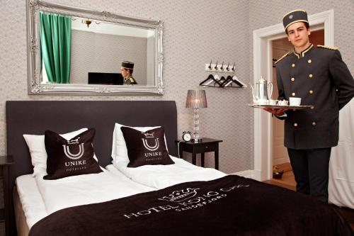 a man in uniform standing next to a bed at Hotel Kong Carl - Unike Hoteller in Sandefjord