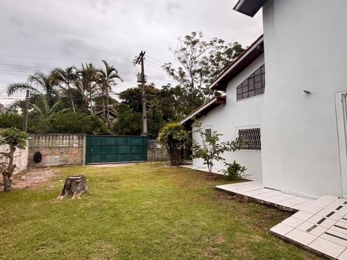 a yard next to a white house with a green gate at Beach House Dunas da Joaquina in Florianópolis