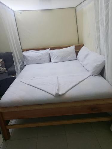 Una cama con sábanas blancas y almohadas. en Alicia Studio, en Mtwapa