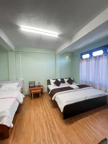 ein Schlafzimmer mit zwei Betten und einem Tisch und einem Fenster in der Unterkunft Hotel Tashi Tseleng in Tawang