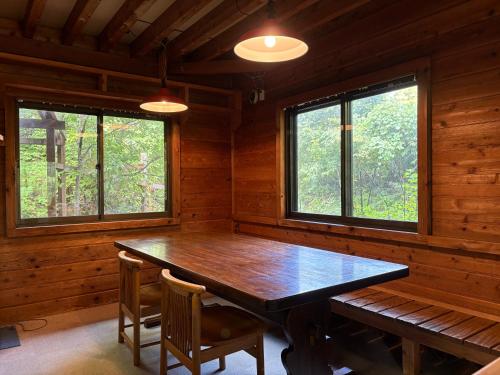 a dining room with a wooden table and two windows at 蔵王ペンション kobaya in Kaminoyama