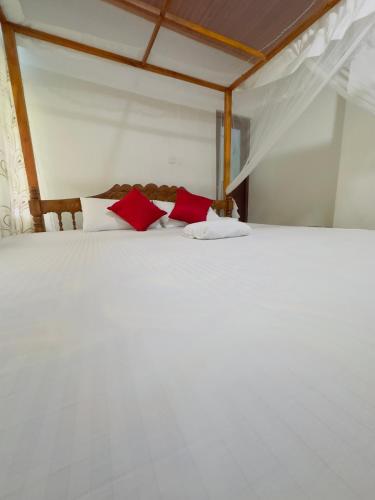 a bedroom with a white bed with red pillows at Goyambokka Richard Home Stay in Tangalle