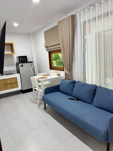 a living room with a blue couch and a kitchen at Baan Trok Bedroom Studio Maikhao in Mai Khao Beach