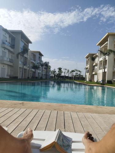 a person laying on a deck next to a swimming pool at Apartment in residence CASABAY in Sidi Rahal