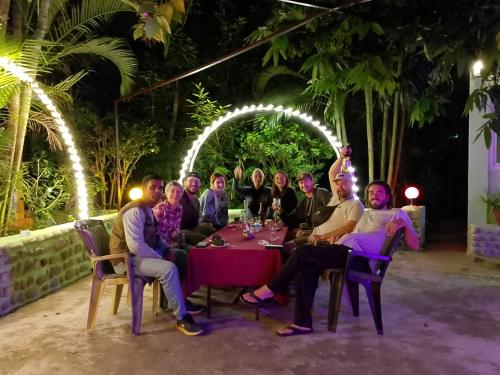 een groep mensen die 's nachts aan een tafel zitten bij Hotel Rhino Land-Sauraha Family Home in Sauraha