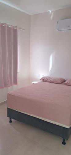 a bed in a white room with a pink bedspread at Casa de Praia Nova, 3 quartos, 1 Suíte, com quintal privativo, em condomínio, muito bem Localizado in Porto Seguro