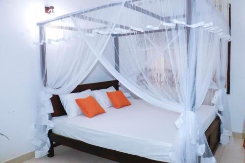 a bedroom with a canopy bed with orange pillows at Thisaru Homestay in Weligama