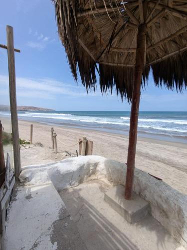 ein Strand mit einem Strohschirm und dem Meer in der Unterkunft cozy studio in Máncora