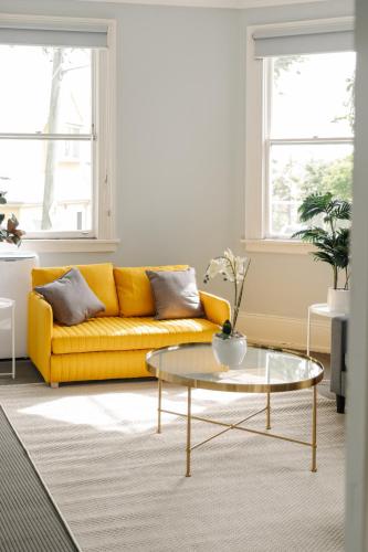 a living room with a yellow couch and a glass coffee table at Chic 2BR Terrace w City and Harbour Bridge Views in Sydney
