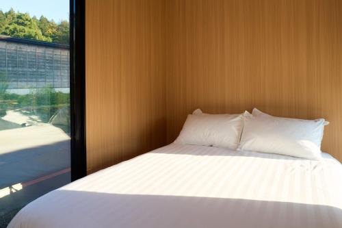 a bed with white pillows and a large window at Kirisawabase Tiny House by Tiny Away in Nagaoka