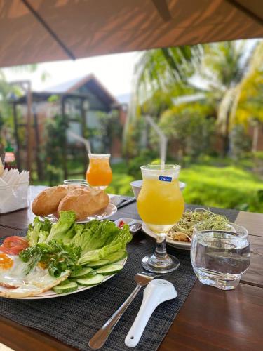 a table with two plates of food and two glasses of orange juice at Biển Tôm ốc Homestay Bến Tre - Hồ Bơi & BBQ Garden 