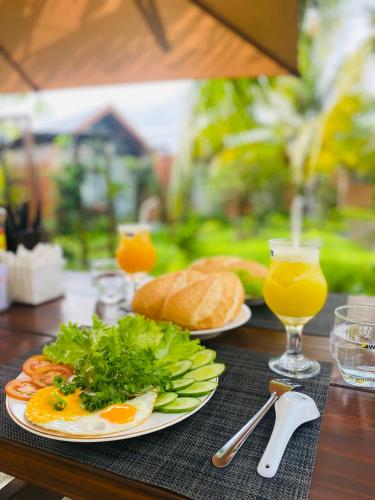 a table with two plates of food and a glass of orange juice at Biển Tôm ốc Homestay Bến Tre - Hồ Bơi & BBQ Garden 