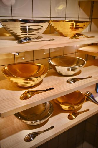 a shelf filled with gold bowls and spoons at ご当地ラーメン食べ放題 "The RAMEN HOTEL" -京都嵐山- in Kyoto
