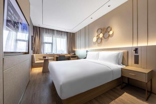 una camera da letto con un grande letto bianco e una scrivania di Orange Hotel Shanghai Meilong Wanhui International Plaza a Shanghai