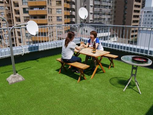 two women sitting at a table on a balcony with green grass at J-Hoppers Hiroshima Guesthouse in Hiroshima