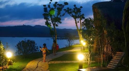 a woman walking down a path near a lake at night at Cô Tô Village in Ðiền Xá
