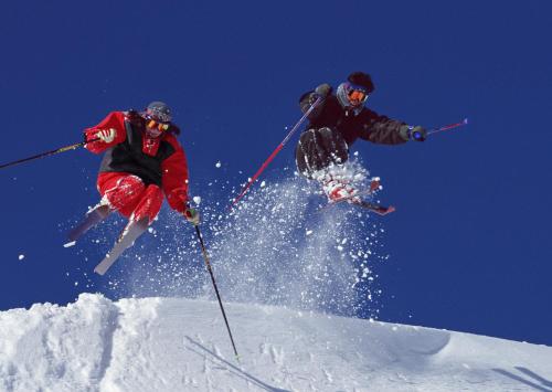 two people jumping in the air on skis in the snow at Blue Ridge Hotel in Toyooka