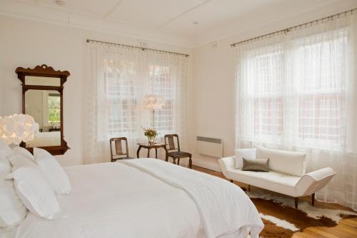 a white bedroom with a large bed and a chair at Mollisons in Kyneton
