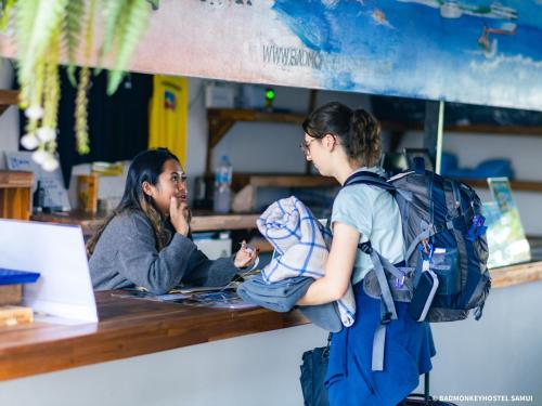 twee vrouwen aan een tafel met een laptop bij Bad Monkey Samui Hostel in Chaweng Beach