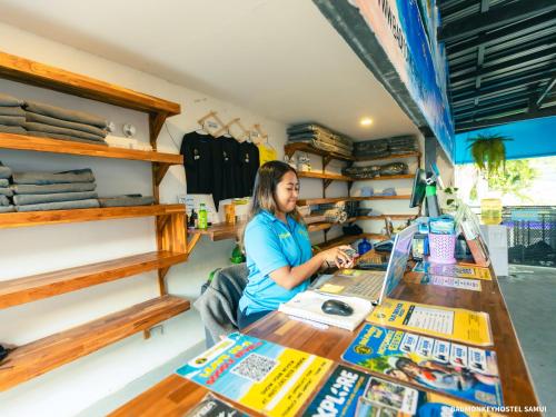 uma mulher sentada à mesa em uma loja em Bad Monkey Samui Hostel em Chaweng