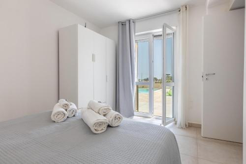 a white bedroom with towels on a bed with a window at Villa Serenella in Carovigno