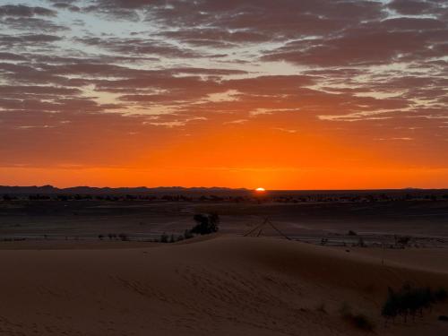 a sunset in the desert with the sun setting at Family Berber Camp in Merzouga