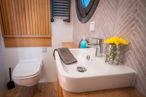 ein Waschbecken im Badezimmer mit Toilette und einer Vase mit gelben Blumen in der Unterkunft Adventurous Water House Emsel Woma in Fürstenberg-Havel