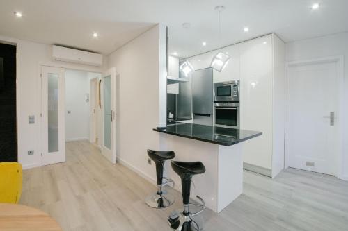 a kitchen with white walls and a counter with stools at Apartamento do Sol, Lobão 