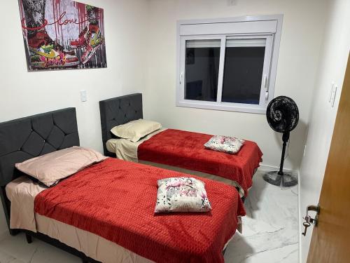 a bedroom with two beds with red sheets and a window at Casa completa para relaxar com a família in Passo De Torres