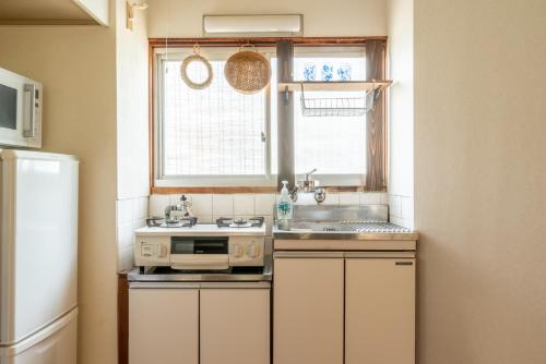 eine Küche mit weißen Schränken und einer Spüle und einem Fenster in der Unterkunft GUEST HOUSE Hotori in Ōtsu