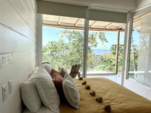 - une chambre dotée d'un lit avec des oreillers et d'une grande fenêtre dans l'établissement Ocean View Jungle Nest - 2min From The Beach, à Santa Teresa