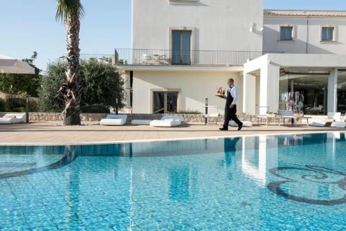 a man in a suit walks by a swimming pool at Pietre Nere Resort & Spa in Modica