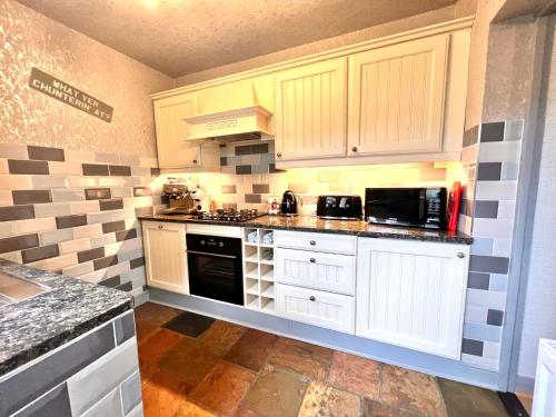 a kitchen with white cabinets and black appliances at Wharfe View Cottage Ilkley in Ilkley