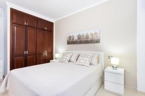ein weißes Schlafzimmer mit einem weißen Bett und Holzschränken in der Unterkunft Brisa - Armonía Park, Bajamar in El Puertito