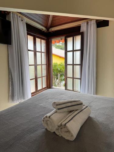 a bed with two towels on it in a room with windows at Pousada Kaianoá in Arraial do Cabo
