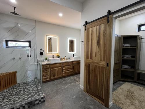 a bathroom with two sinks and a shower and a wooden door at Emerald Blue Villa - Modern 2BR Villa with Rooftop Lounge Pool in Placencia Village