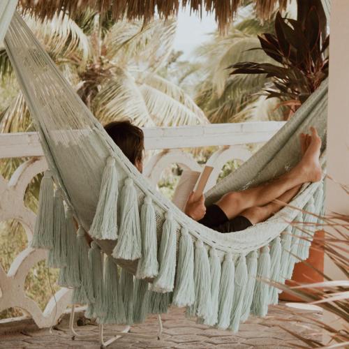 a man laying in a hammock reading a book at Hotel Flor de Maria - Adults Only in Puerto Escondido