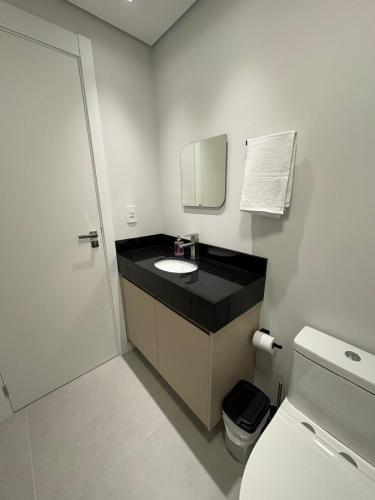 a bathroom with a sink and a mirror and a toilet at Loft com Piscina no Rooftop centro de Blumenau in Blumenau