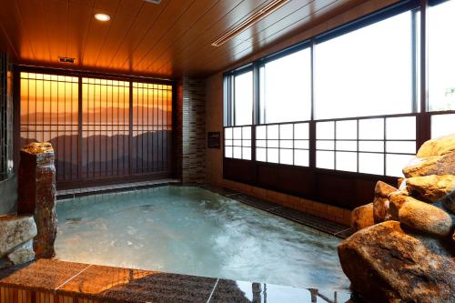 a hot tub in a room with windows at Dormy Inn Nagano in Nagano