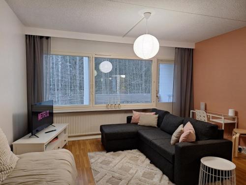 Una sala de estar con un sofá negro y un televisor. en Ihana kaksio lähellä luontoa!, en Tampere